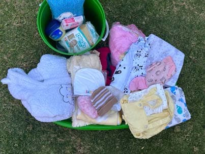 A prepared baby package of blankets, clothing and toiletries in a green tub